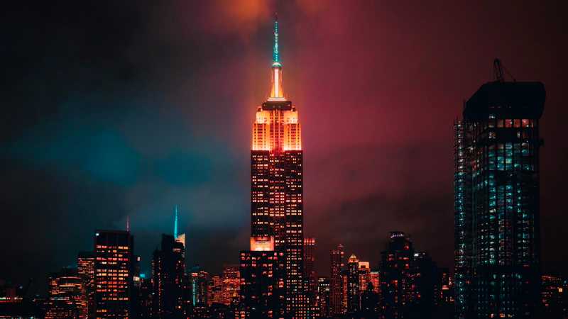 Skyline-ul din New York noaptea, cu Empire State Building luminat între alte clădiri