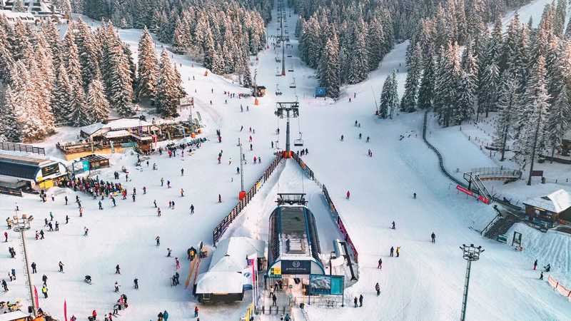 Vedere aeriană a unei pârtii de schi din Serbia, cu telescaun, schiori și brazi înzăpeziți