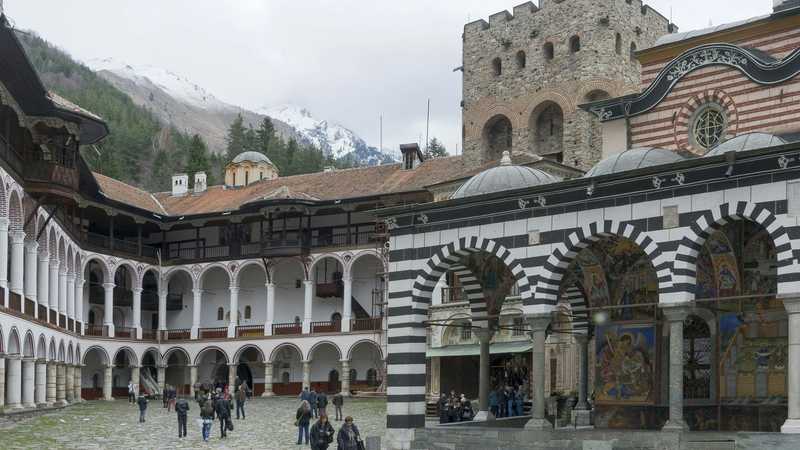 Mănăstirea Rila, cu ziduri și acoperișuri, în fața munților împăduriți din Bulgaria