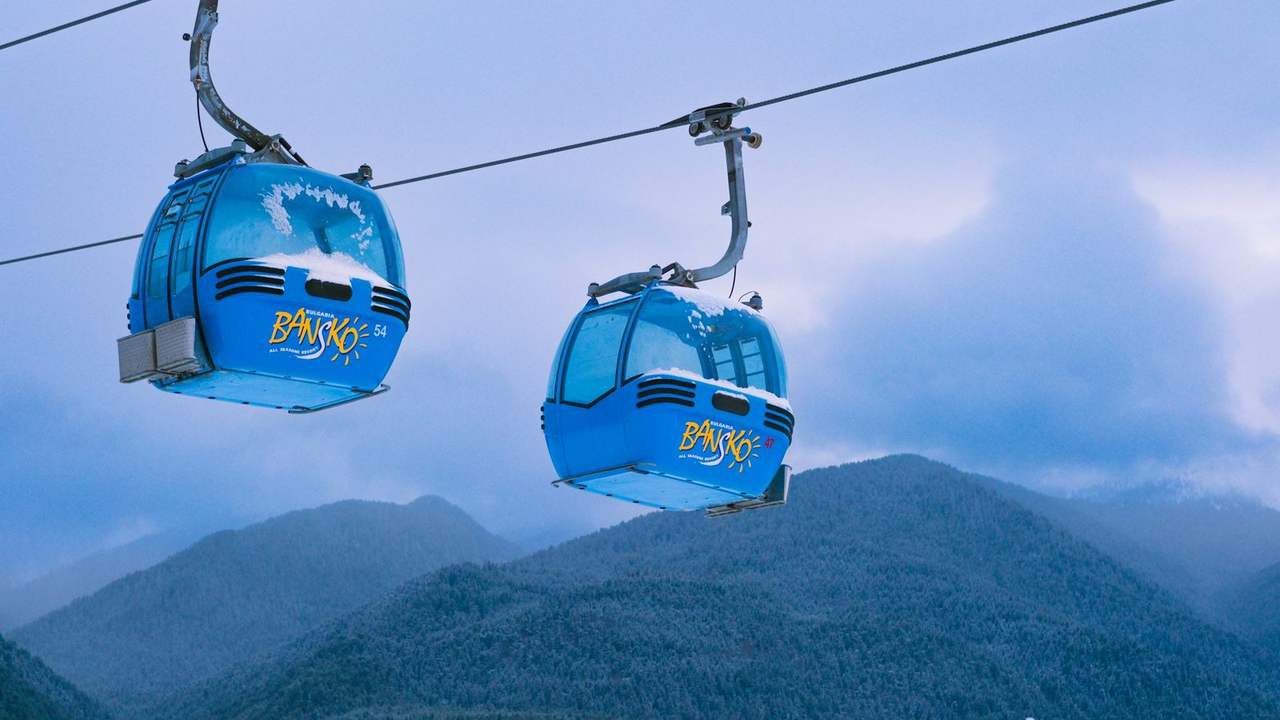 Două cabine albastre ale telegondolei din Bansko, cu munții Pirin înzăpeziți în spate